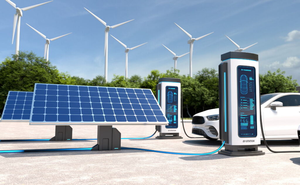 Dois postos de carregamento de veículos elétricos ligados por cabo a painéis solares, com turbinas eólicas ao fundo e um automóvel branco a carregar