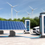 Dois postos de carregamento de veículos elétricos ligados por cabo a painéis solares, com turbinas eólicas ao fundo e um automóvel branco a carregar